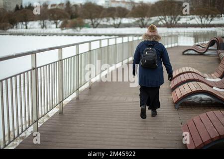 Donna cammina lungo il lungomare in inverno. Parco cittadino. Ragazza cammina da sola in città. Foto Stock