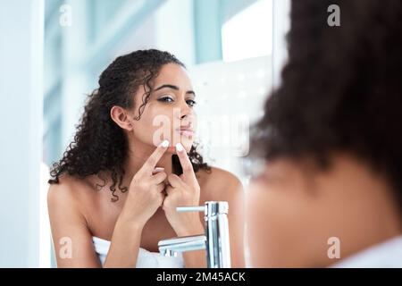 Non sei qui per stare. una bella giovane donna che stringe un pimple mentre guarda nello specchio. Foto Stock