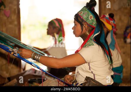 Due ragazze Padaung (Karen o Kayan Lahwi) che indossano gli anelli di metallo tradizionali intorno al suo collo, lavorando ad una tessitura in un villaggio galleggiante aperto., Myanmar. Foto Stock