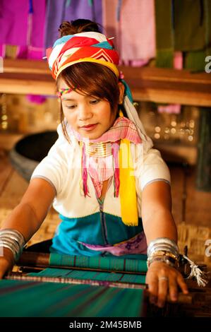 Due ragazze Padaung (Karen o Kayan Lahwi) che indossano gli anelli di metallo tradizionali intorno al suo collo, lavorando ad una tessitura in un villaggio galleggiante aperto., Myanmar. Foto Stock