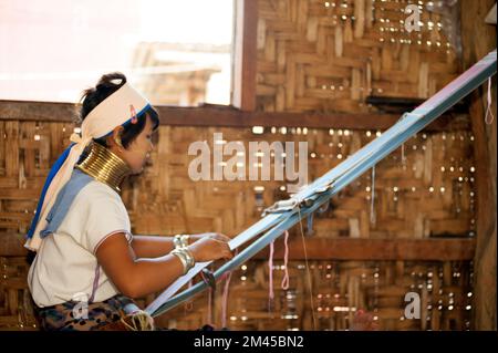 Due ragazze Padaung (Karen o Kayan Lahwi) che indossano gli anelli di metallo tradizionali intorno al suo collo, lavorando ad una tessitura in un villaggio galleggiante aperto., Myanmar. Foto Stock