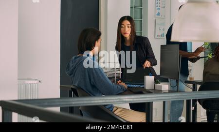 Team di amministratori di database che analizzano il codice sorgente sul monitor del computer, confrontando gli script dei dati in un ufficio di agenzia occupato. Due programmatori cloud che effettuano il debug dell'algoritmo nell'ufficio di sviluppo software. Foto Stock