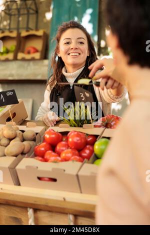 Sorridente e amichevole proprietario del negozio di frutta e verdura biologica che offre ai clienti di assaggiare diverse varietà di mele al mercato alimentare. Positiva femmina contadina che vende prodotti freschi locali Foto Stock