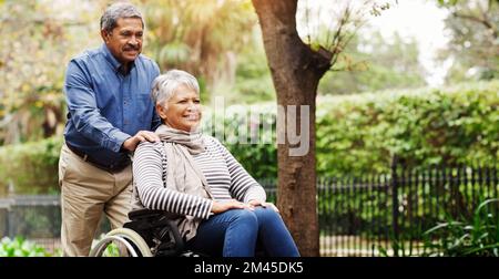 HES mi sostiene e mi spinge sempre in avanti. un uomo anziano affettuoso che spinge la sua sedia a rotelle ha legato la moglie intorno al parco. Foto Stock