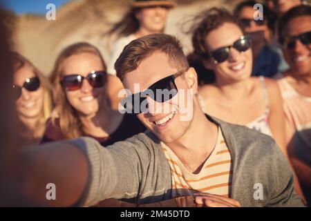 Fai un selfie e lascia che i momenti migliori rotolino. Ritratto corto di un bel giovane che prende un selfie con i suoi amici in spiaggia. Foto Stock