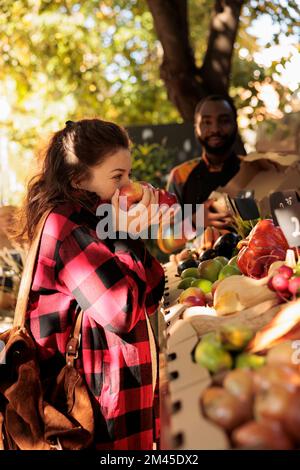 Acquirente femmina scegliendo prodotti freschi per piccole imprese, odorando mele biologiche colorate in scatole. Donna che si prepara ad acquistare frutta e verdura al mercato bio-alimentare naturale, vari prodotti. Foto Stock