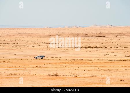 Auto fuoristrada che si muove su strada di ghiaia nel deserto infinito della Namibia in una giornata di sole Foto Stock