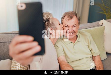 Senior, bacio e selfie telefono di una coppia con amore, cura e felicità su un divano soggiorno. Felice, sorriso e matrimonio di una moglie e di un uomo insieme Foto Stock