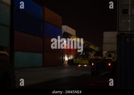 Raggiungere l'impilatore durante il funzionamento. Caricatore di contenitori con impilatore a scorrimento durante il lavoro notturno. Terminale contenitore porta industriale. Impilatore di contenitori nella porta su Foto Stock