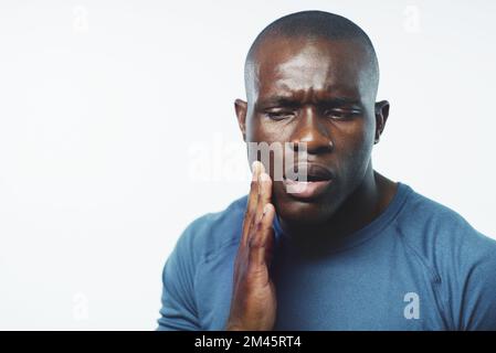 Qualcosa non si sente proprio qui. Studio di un giovane che soffre di mal di denti su sfondo grigio. Foto Stock