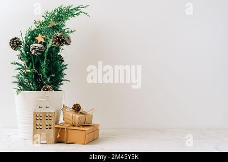 Albero di Natale in miniatura naturale creativo in vaso su tavolo di legno con scatole regalo e sfondo bianco. Biglietto di auguri natalizio con spazio per la copia. Felice nuovo Foto Stock