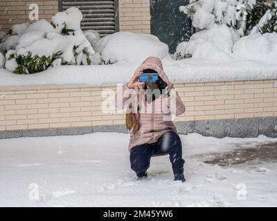 Donna che scatta foto con un telefono cellulare in strada durante una nevicata. Concetto invernale. Foto Stock