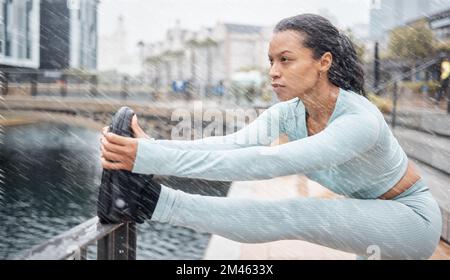 Fitness, pioggia e donna che si allungano all'aperto per il benessere muscolare, la salute e l'energia in inverno con allenamento, corsa o allenamento. Città, Amsterdam e. Foto Stock
