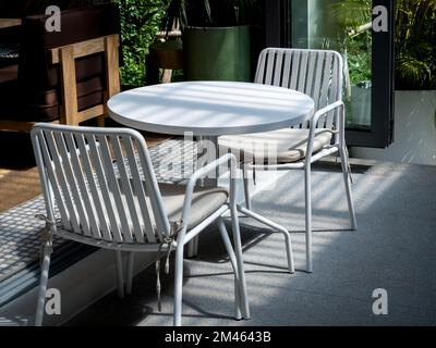 Piccolo tavolo all'aperto allestito presso il ristorante o la caffetteria. Due sedie vuote con cialde e tavolo rotondo bianco vuoto di fronte alla caffetteria. Foto Stock