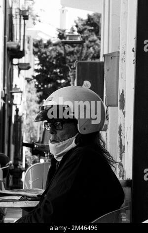 Scala di grigi verticale di un vecchio che indossa una maschera e un casco sullo sfondo sfocato Foto Stock