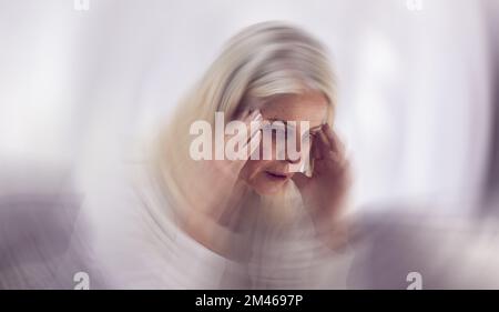 Donna anziana, mal di testa e vertigini movimento sfocato sul divano per la salute mentale, lo stress e il rischio per la salute. Persona anziana, stanca e che soffre di emicrania per Foto Stock