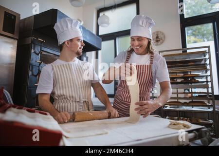 Uomo con giù sindromi aiutare a preabbinare il pane in panetteria con il suo collega. Concetto di integrazione delle persone con disabilità nella società. Foto Stock