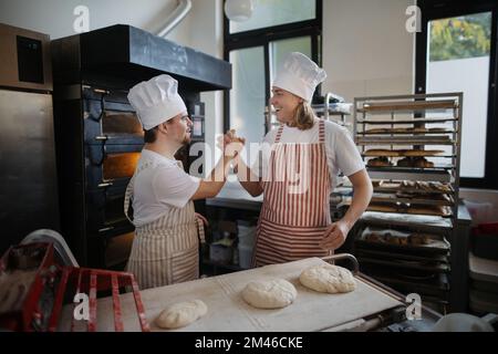 Uomo con giù sindromi aiutare a preabbinare il pane in panetteria con il suo collega. Concetto di integrazione delle persone con disabilità nella società. Foto Stock