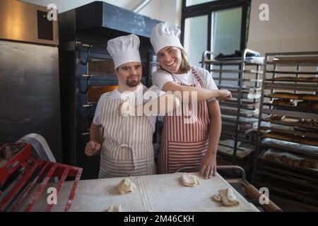 Ritratto dell'uomo con sindrome di Down e il suo collega in panetteria. Concetto di integrazione delle persone con disabilità nella società. Foto Stock