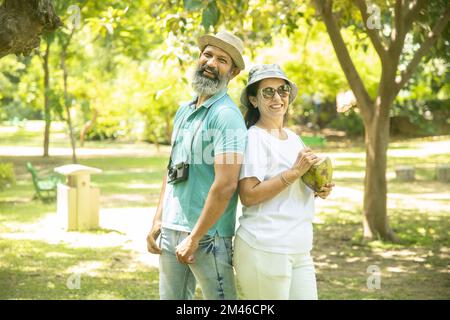 Coppia matura indiana felice che indossa un cappello con acqua di cocco al parco estivo. anziani che godono la vita di pensione. Foto Stock