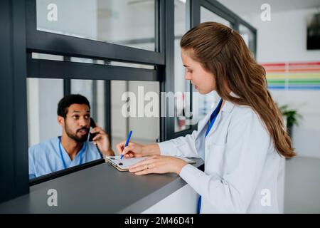 Giovane medico che parla alla reception dell'ospedale con la sua collega. Foto Stock