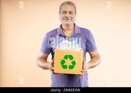 Felice uomo anziano indiano ecologico che tiene una scatola piena di bottiglie di plastica per il riciclaggio. Protezione ambientale, concetto di giornata della terra Foto Stock