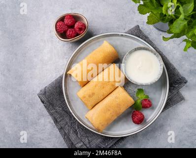 Crepes fatte in casa con lampone e panna acida su un piatto su uno sfondo chiaro con primo piano di menta fresca. Concetto di cibo sano. Vista dall'alto e spazio di copia Foto Stock