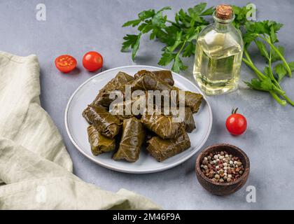 Dolma. Foglie d'uva ripiene (cucina tradizionale caucasica, turca, greca) su un piatto blu con erbe fresche su sfondo chiaro con olio di oliva Foto Stock