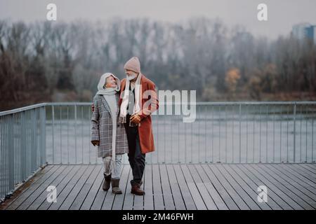 Elegante coppia anziana a piedi vicino al fiume, durante la fredda giornata invernale. Foto Stock