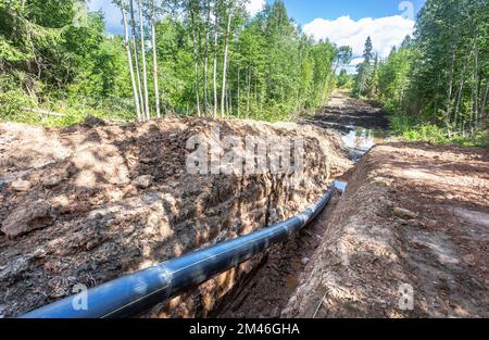 Posa di un tubo di gas in plastica in una trincea in estate. Il gasdotto è installato sotto terra Foto Stock