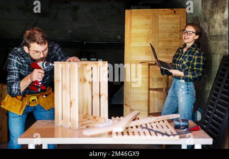 Giovane coppia che lavora insieme nel loro uomo di Falegnameria di piccola impresa che fa la donna della scatola di legno usando il laptop. Foto Stock