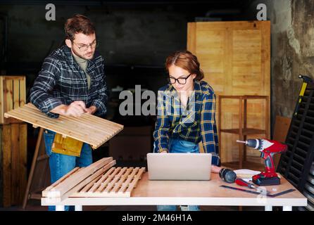 Due persone moglie e marito che lavorano in una propria officina di Falegnameria guardando i lavori di pianificazione del computer portatile. Foto Stock