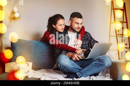 Felice coppia giovane insieme utilizzando il loro portatile online shopping mentre a casa e godersi le vacanze di natale. Foto Stock