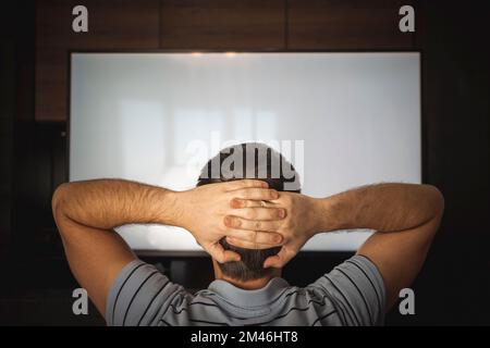 Uomo che guarda la televisione con schermo bianco girato dietro le spalle dei modelli. Ragazzo rilassante seduta su una casa Couch guardando alla TV. Foto Stock