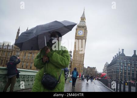 Una donna si rifugia sotto un ombrello mentre cammina sotto la pioggia lungo il Westminster Bridge, nel centro di Londra. Data immagine: Lunedì 19 dicembre 2022. Foto Stock