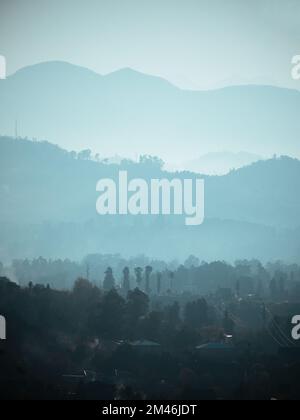 Strati di silhouette di catene montuose in nebbia, nebbia o fumo. Banner verticale natura paesaggio in blu. Foto Stock