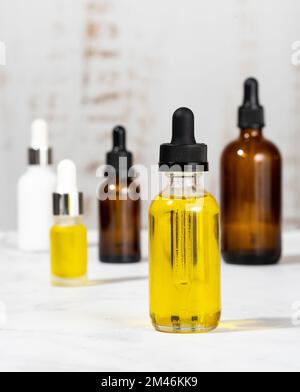 Un set di cosmetici organici in fiale di vetro con contagocce per la cura della pelle e dei capelli. Bottiglie con oli essenziali sul tavolo cosmetico in bagno. Foto Stock