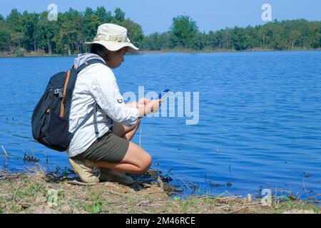 Donna ambientalista che utilizza il telefono cellulare per registrare l'analisi degli agenti patogeni nelle acque naturali. Concetto di acqua ed ecologia Foto Stock