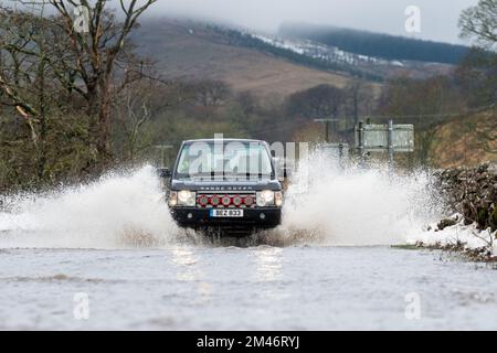 Yorkshire Dales, Regno Unito, 19 dic 2022 - Meteo - inondazioni in flash dopo il rapido scongelamento ha visto il viaggio interrotto intorno alle Yorkshire Dales, in quanto il terreno congelato non è stato in grado di assorbire le acque scioglienti della neve. Questi veicoli hanno lottato attraverso l'acqua in aumento mentre viaggiavano verso Hawes nello Yorkshire Dales, Regno Unito. Credit: Wayne HUTCHINSON/Alamy Live News Foto Stock