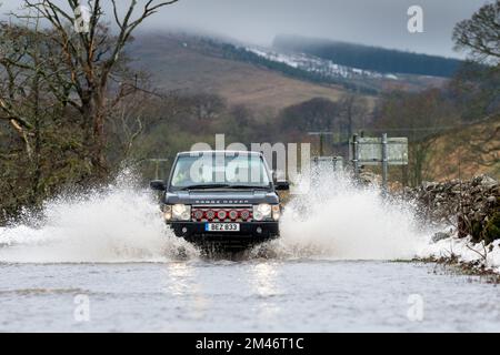 Yorkshire Dales, Regno Unito, 19 dic 2022 - Meteo - inondazioni in flash dopo il rapido scongelamento ha visto il viaggio interrotto intorno alle Yorkshire Dales, in quanto il terreno congelato non è stato in grado di assorbire le acque scioglienti della neve. Questi veicoli hanno lottato attraverso l'acqua in aumento mentre viaggiavano verso Hawes nello Yorkshire Dales, Regno Unito. Credit: Wayne HUTCHINSON/Alamy Live News Foto Stock