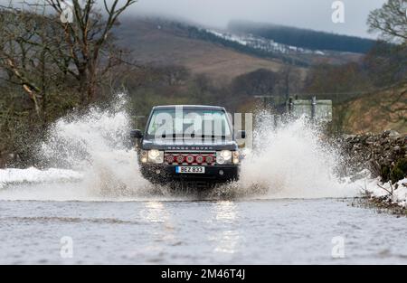 Yorkshire Dales, Regno Unito, 19 dic 2022 - Meteo - inondazioni in flash dopo il rapido scongelamento ha visto il viaggio interrotto intorno alle Yorkshire Dales, in quanto il terreno congelato non è stato in grado di assorbire le acque scioglienti della neve. Questi veicoli hanno lottato attraverso l'acqua in aumento mentre viaggiavano verso Hawes nello Yorkshire Dales, Regno Unito. Credit: Wayne HUTCHINSON/Alamy Live News Foto Stock