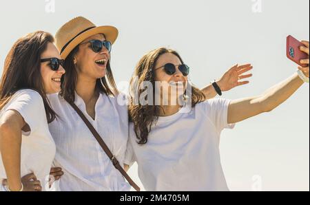 Tre belle donne adulte felici in occhiali da sole che prendono selfie all'aperto. Foto Stock