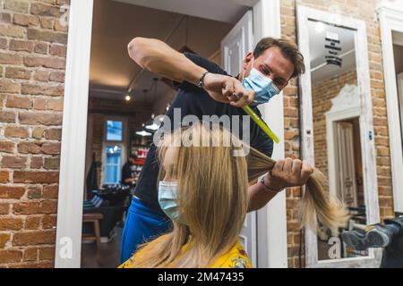 Acconciatura pandemica. Cliente e parrucchiere in maschere. Cliente felice che visita il salone del parrucchiere durante la pandemia. Protezione contro i virus. Foto di alta qualità Foto Stock