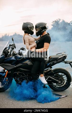 Uomo e donna in caschi moto vicino alla moto con fumo colorato Foto Stock