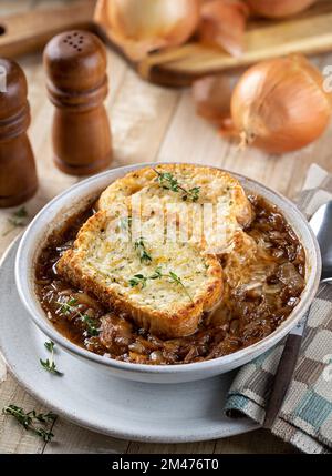 Zuppa francese di cipolle con baguette di formaggio tostato guarnita con timo su un rustico tavolo di legno Foto Stock