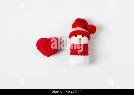 Un pupazzo di neve lavorato a maglia e un cuore rosso su sfondo grigio. Concetto di vacanza invernale di Natale Foto Stock