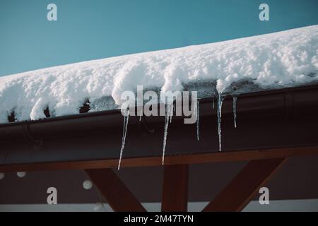 Ciclicini affilati e neve fusa appesa a grondaie di tetto. Bellissimi ghiaccioli trasparenti che scivolano lentamente su un tetto. Foto Stock