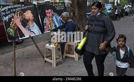 Mumbai, India. 19th Dec, 2022. Una donna e un bambino a piedi da un artista della scuola d'arte di Gurukul mettendo ultimi tocchi a un dipinto di Lionel messi baciare il trofeo di Coppa del mondo, il dipinto è un complimento per l'Argentina per aver vinto la Coppa del mondo di calcio. L'Argentina ha vinto la Coppa del mondo FIFA (Federation Internationale de Football Association) dopo 36 anni dal loro ultimo trionfo sulla Germania occidentale nel 1986. Credit: SOPA Images Limited/Alamy Live News Foto Stock