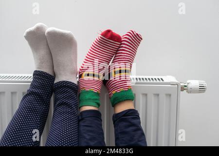 Madre e bambino che scalda i piedi vicino al riscaldatore a casa, primo piano Foto Stock