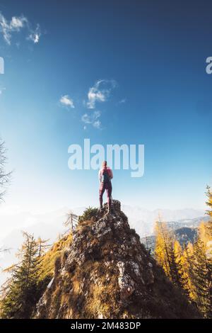 Foto verticale, vista posteriore di una donna escursionista in piedi in cima alla roccia in una soleggiata giornata autunnale guardando la vista dall'alto Foto Stock